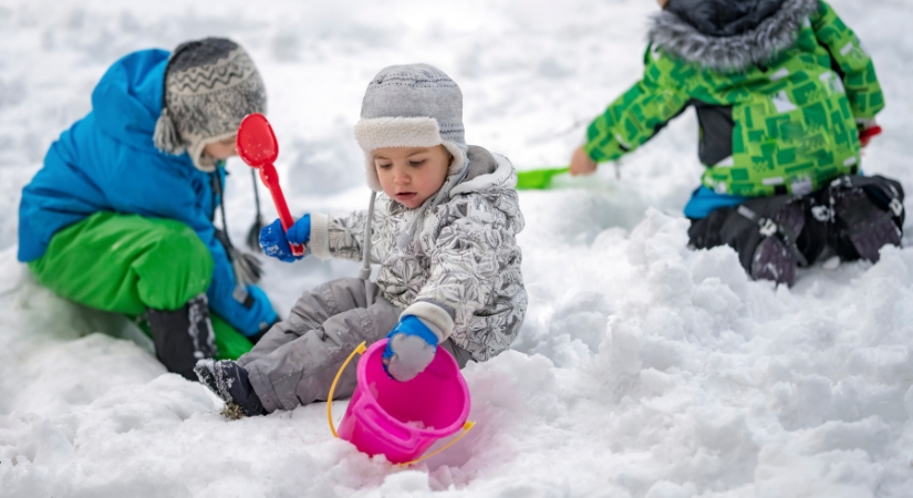 young child playing in the snow holding a bucket and spade.